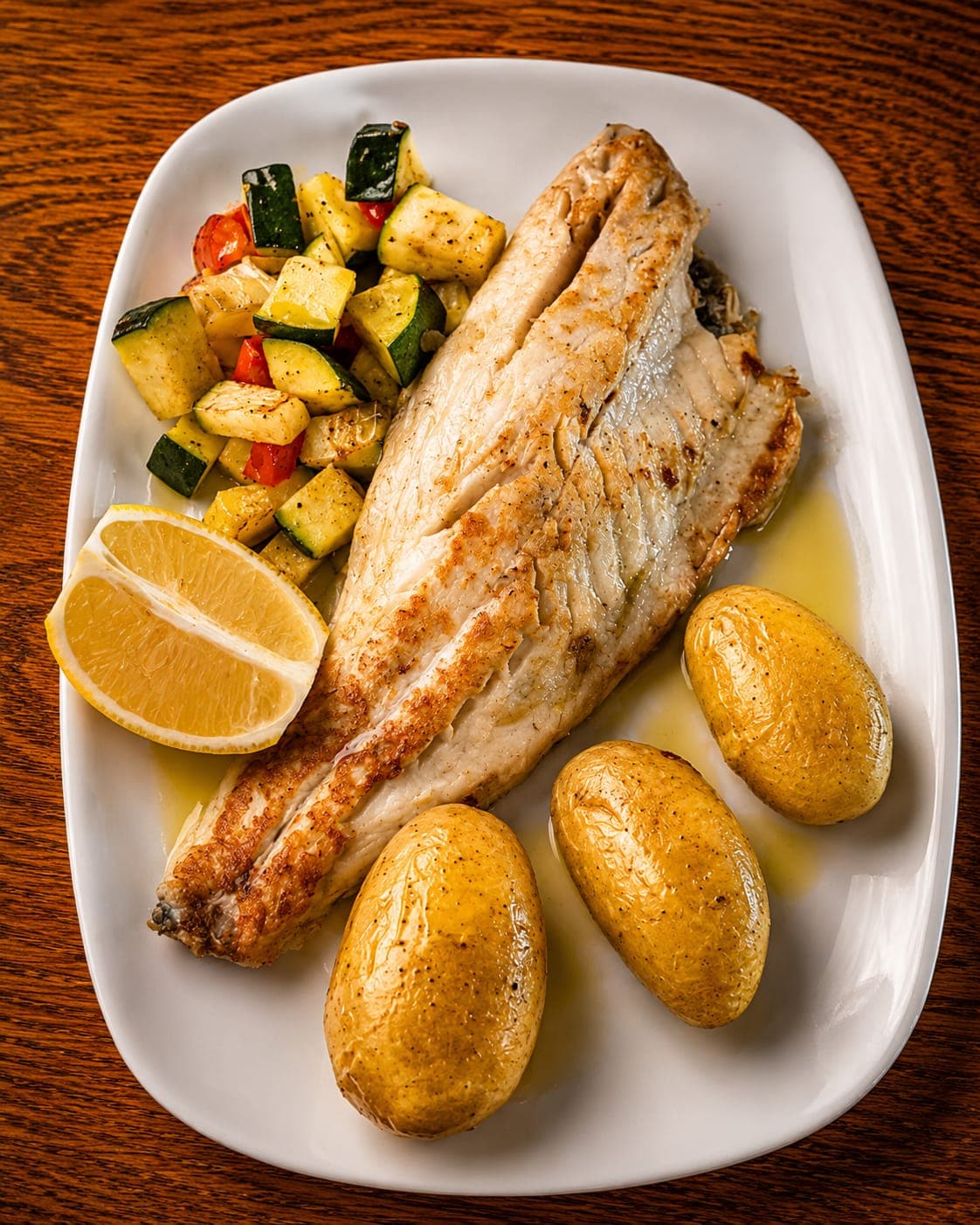 Filete de pescado a la plancha con patatas rústicas, verduras de temporada y limón